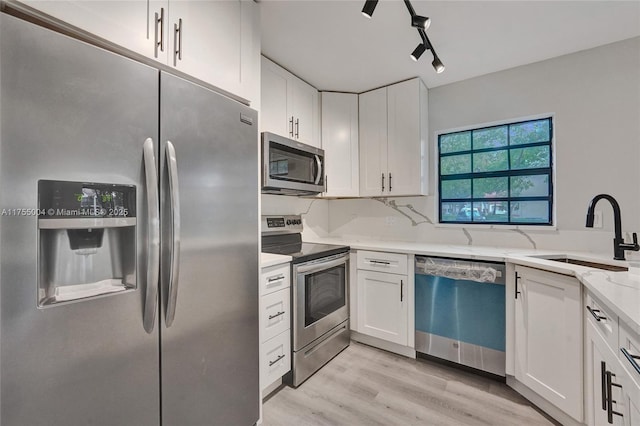 kitchen featuring light stone counters, stainless steel appliances, a sink, white cabinets, and light wood-type flooring