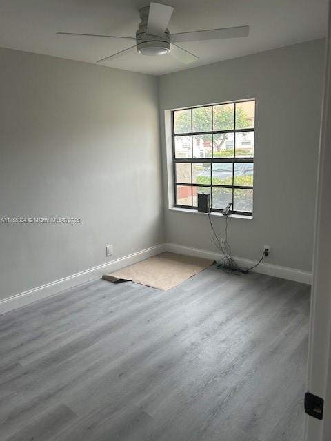 spare room featuring wood finished floors, a ceiling fan, and baseboards