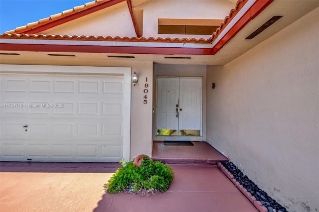 doorway to property with concrete driveway, a tile roof, and stucco siding