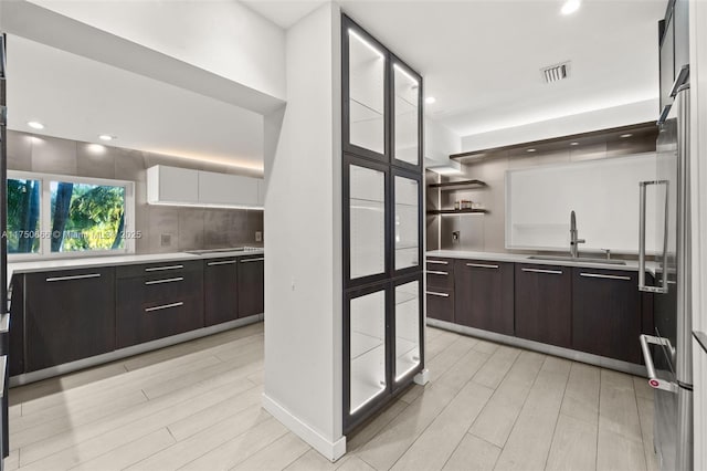 kitchen with light countertops, visible vents, a sink, dark brown cabinets, and light wood-type flooring