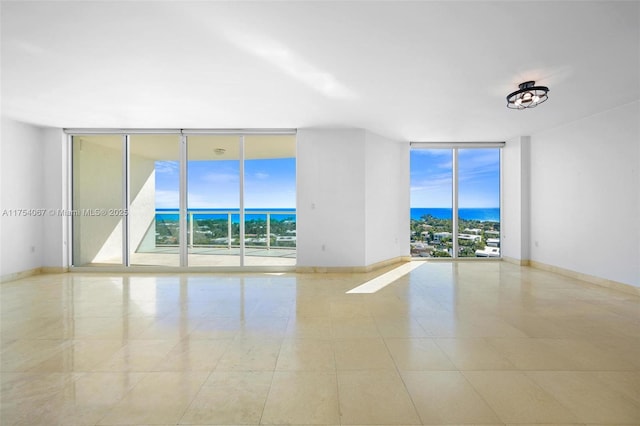 spare room with a water view, baseboards, and floor to ceiling windows