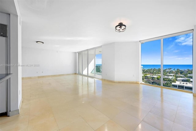 empty room featuring expansive windows, light tile patterned floors, a water view, and baseboards