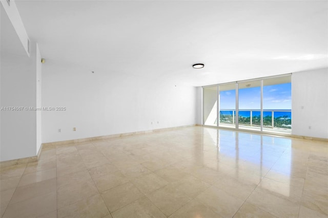 unfurnished room featuring expansive windows, a water view, and baseboards