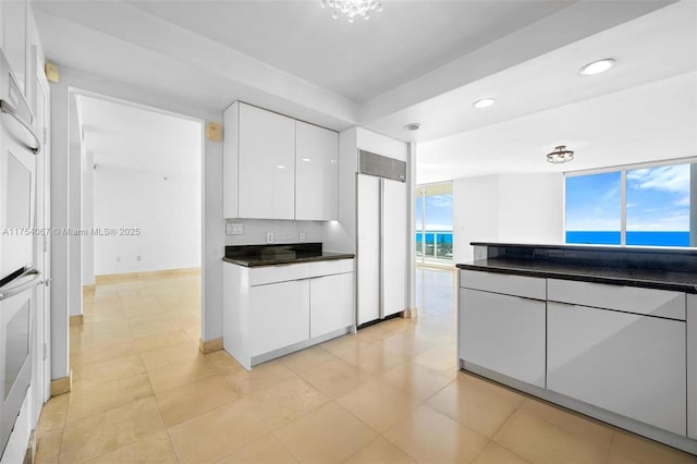 kitchen featuring oven, built in refrigerator, white cabinetry, dark countertops, and modern cabinets