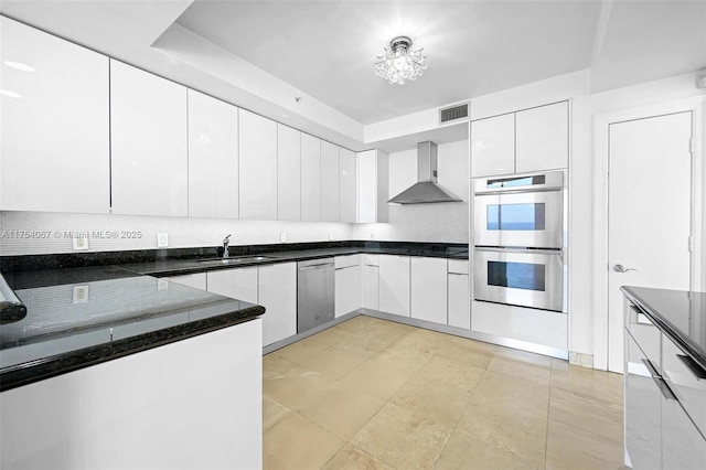 kitchen featuring stainless steel appliances, white cabinets, a sink, and wall chimney range hood