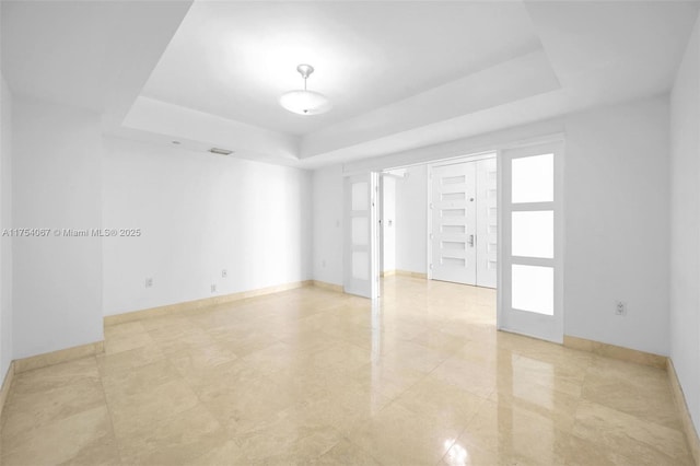 empty room featuring visible vents, baseboards, and a raised ceiling