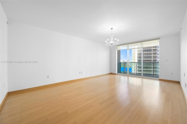 empty room with light wood-type flooring, baseboards, a chandelier, and a wall of windows