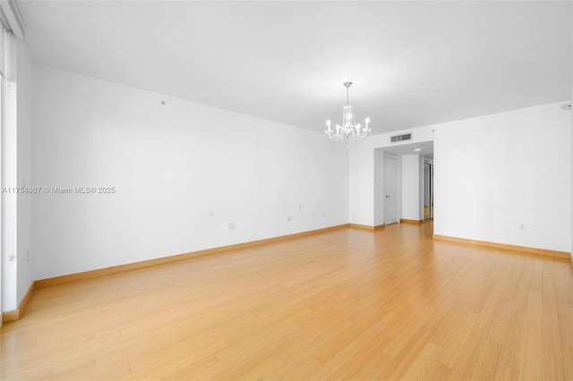 spare room featuring visible vents, light wood-style flooring, baseboards, and an inviting chandelier