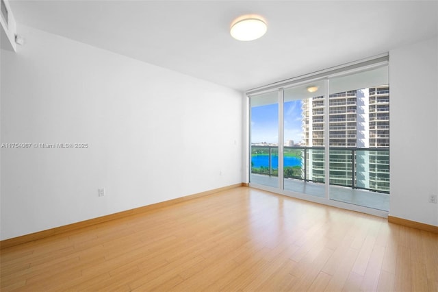 empty room featuring expansive windows, baseboards, and wood finished floors