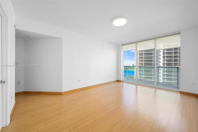 spare room with floor to ceiling windows, light wood-style flooring, and baseboards