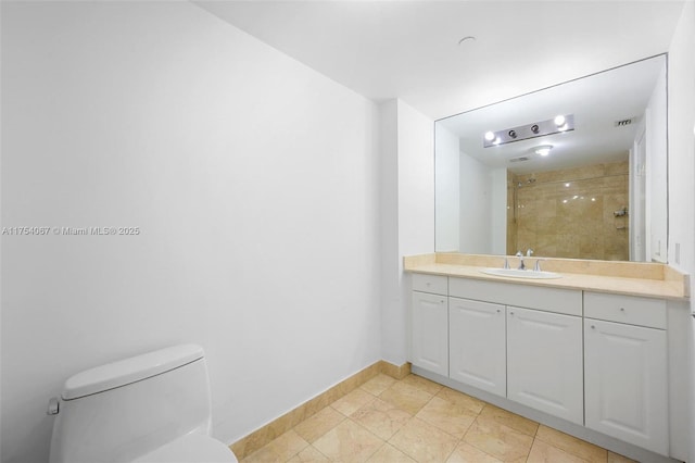 bathroom featuring tile patterned flooring, toilet, vanity, baseboards, and a tile shower