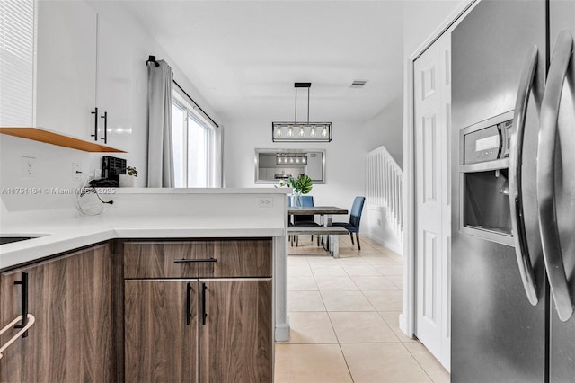 kitchen with light countertops, visible vents, light tile patterned flooring, stainless steel fridge, and a peninsula