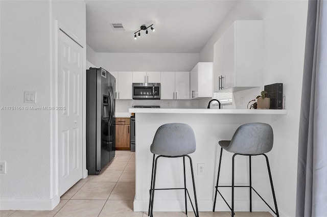 kitchen with a peninsula, visible vents, white cabinets, appliances with stainless steel finishes, and a kitchen bar