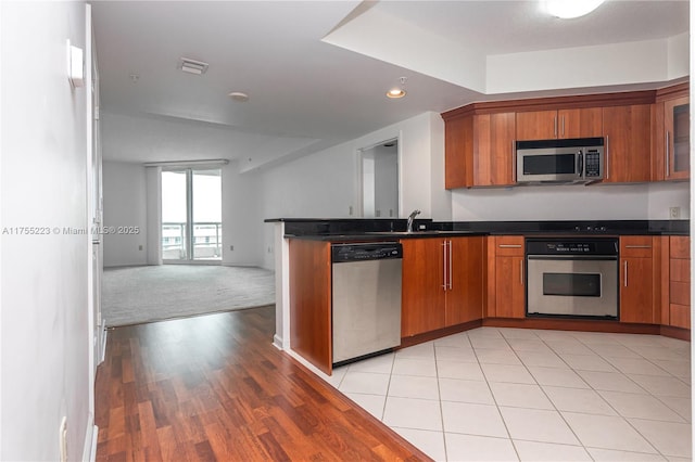 kitchen featuring dark countertops, appliances with stainless steel finishes, brown cabinets, open floor plan, and a peninsula