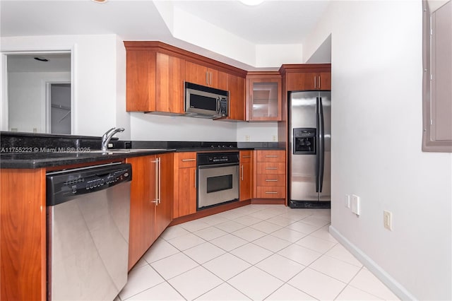 kitchen featuring dark countertops, brown cabinetry, glass insert cabinets, and stainless steel appliances