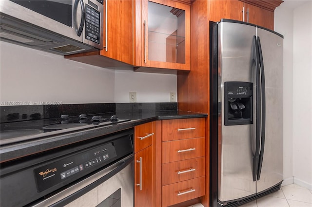 kitchen featuring brown cabinets, light tile patterned floors, appliances with stainless steel finishes, dark stone counters, and baseboards