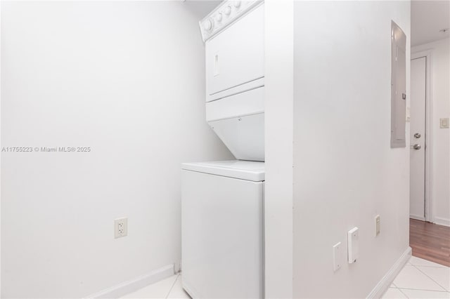 washroom featuring light tile patterned floors, laundry area, stacked washer and clothes dryer, and baseboards