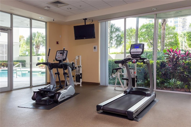 exercise room featuring a paneled ceiling, baseboards, expansive windows, and visible vents