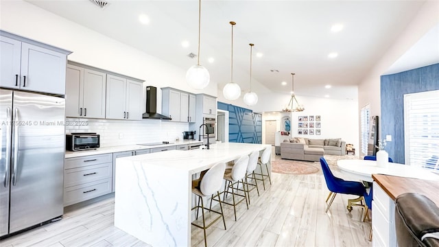 kitchen with stainless steel appliances, gray cabinetry, open floor plan, wall chimney range hood, and a kitchen breakfast bar