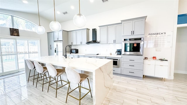 kitchen featuring a breakfast bar, stainless steel appliances, tasteful backsplash, visible vents, and wall chimney exhaust hood