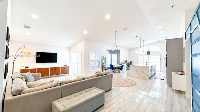 living area with lofted ceiling, an inviting chandelier, light wood-style flooring, and visible vents