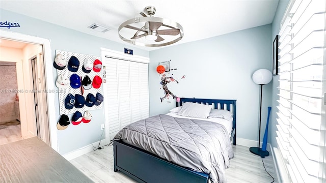 bedroom with baseboards, visible vents, light wood-style flooring, ceiling fan, and a closet