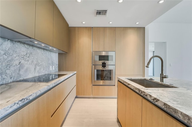 kitchen featuring double oven, visible vents, a sink, and light stone countertops