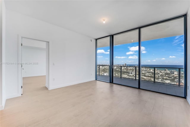 spare room with expansive windows, a water view, wood finished floors, and baseboards