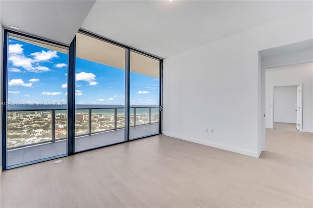 unfurnished room with baseboards, wood finished floors, a water view, a wall of windows, and a view of the beach