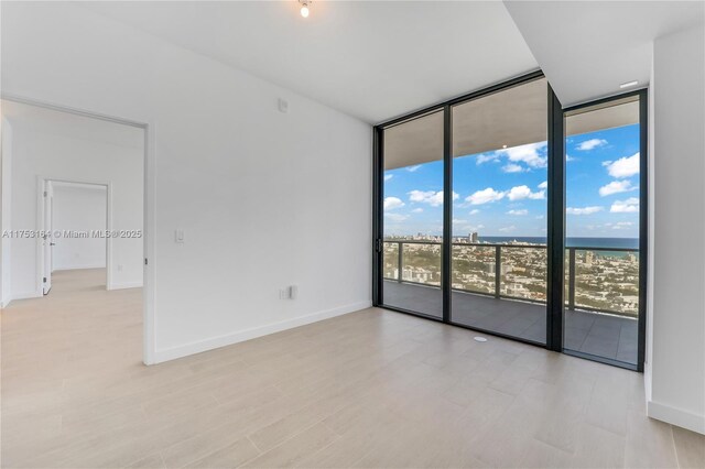 spare room featuring a water view, expansive windows, baseboards, and wood finished floors