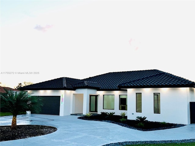 view of front of house featuring a tile roof, an attached garage, driveway, and stucco siding