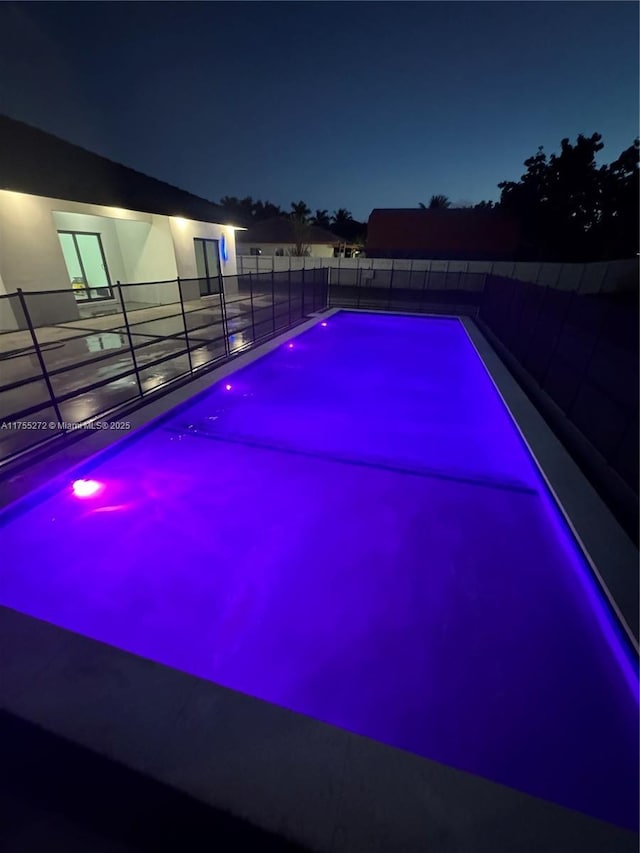 pool at twilight with a fenced in pool and fence