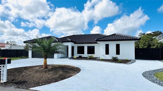 view of front of property with stucco siding, a tiled roof, fence, and curved driveway