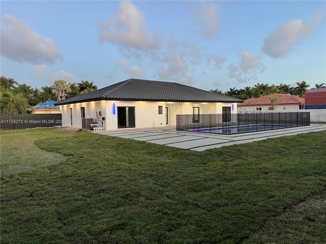 back of property with stucco siding, a tile roof, fence, a yard, and a fenced in pool