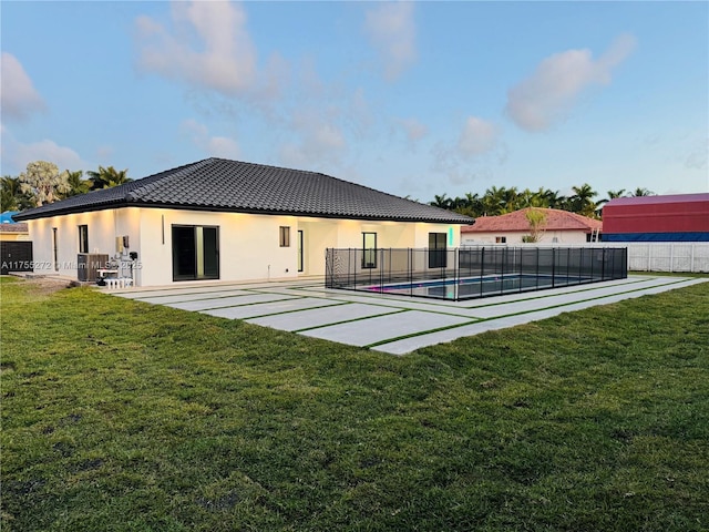 back of house with a fenced in pool, a tiled roof, fence, and a lawn