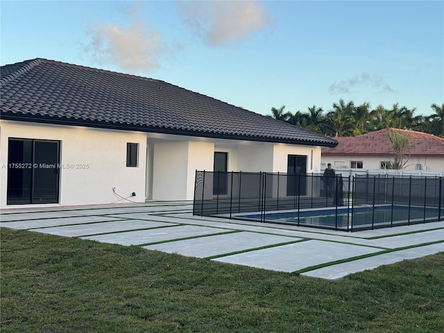 rear view of property featuring stucco siding, a tiled roof, a yard, and fence