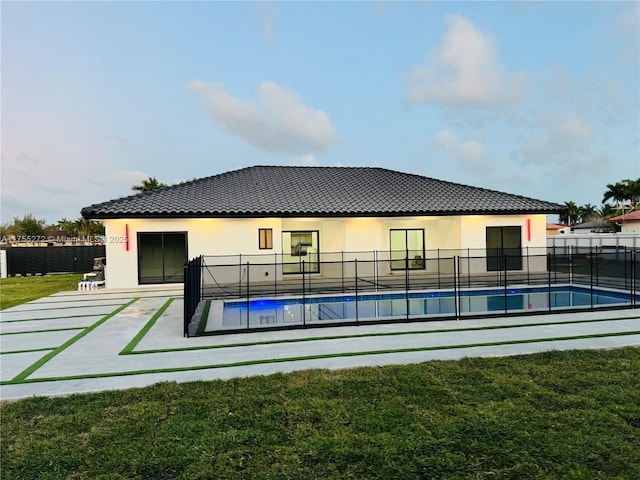 back of house with stucco siding, fence, a yard, a fenced in pool, and a tiled roof