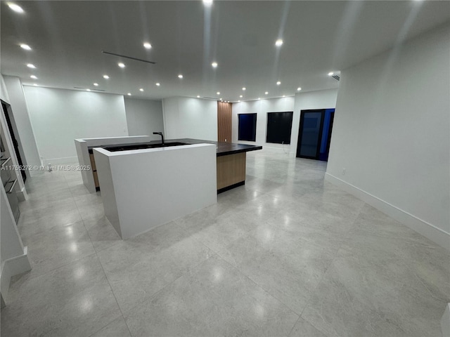 kitchen featuring baseboards, open floor plan, recessed lighting, a large island with sink, and modern cabinets