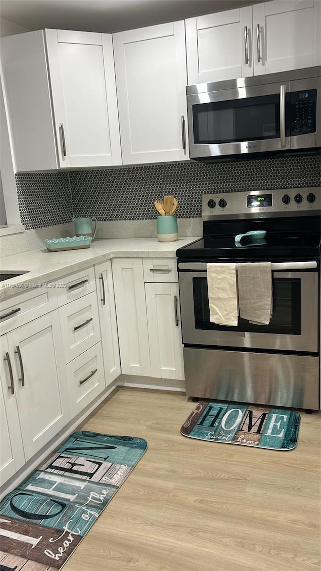 kitchen featuring white cabinets, light wood-type flooring, stainless steel appliances, and backsplash