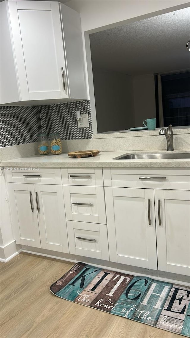 interior space featuring double vanity, decorative backsplash, a sink, a textured ceiling, and wood finished floors