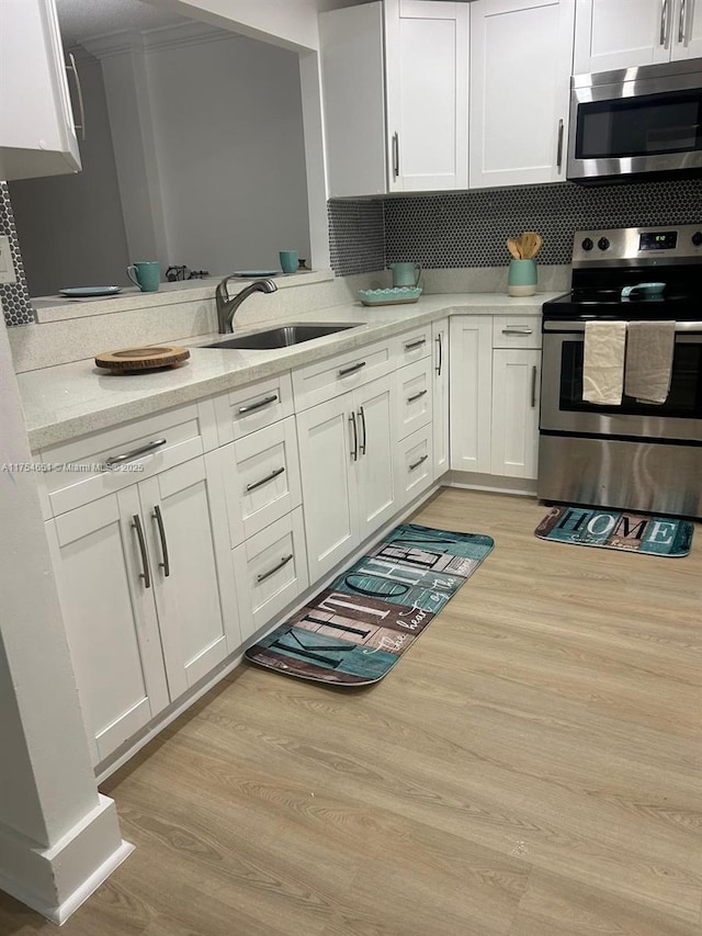 kitchen with appliances with stainless steel finishes, white cabinetry, a sink, and light wood-style flooring