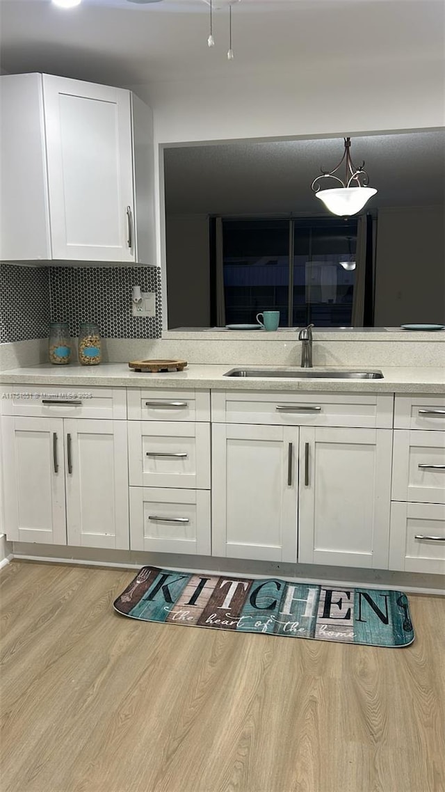 kitchen featuring a sink, white cabinets, light countertops, light wood-type flooring, and decorative backsplash