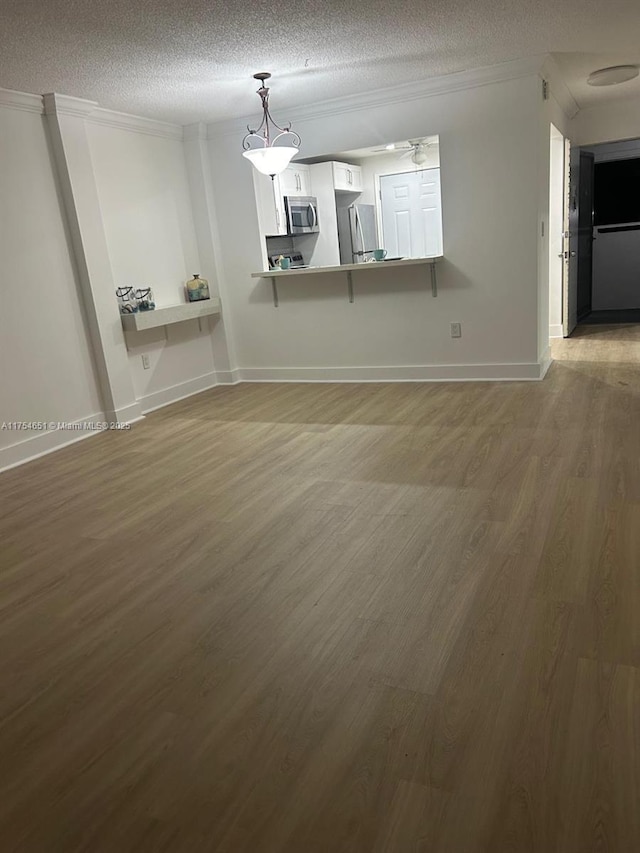 unfurnished room with a textured ceiling, wood finished floors, a ceiling fan, baseboards, and crown molding