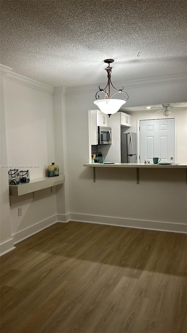 kitchen with a textured ceiling, appliances with stainless steel finishes, dark wood-style flooring, and ornamental molding