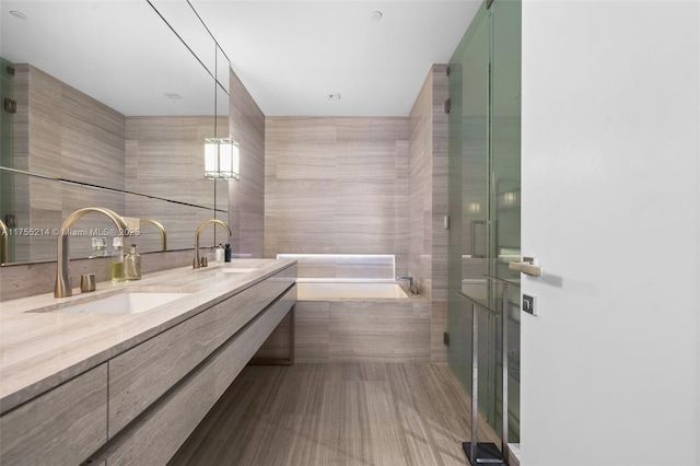 bathroom featuring a garden tub, double vanity, a sink, and tile walls