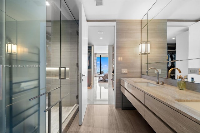 full bathroom featuring a sink, visible vents, a spacious closet, a shower stall, and double vanity