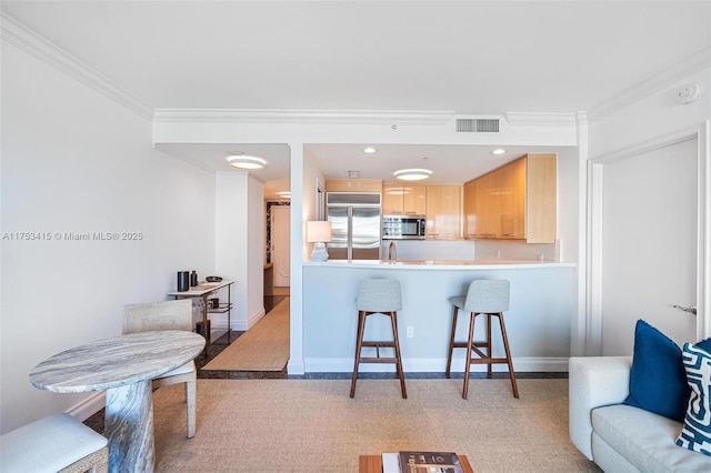 kitchen with ornamental molding, stainless steel appliances, light brown cabinetry, and a breakfast bar