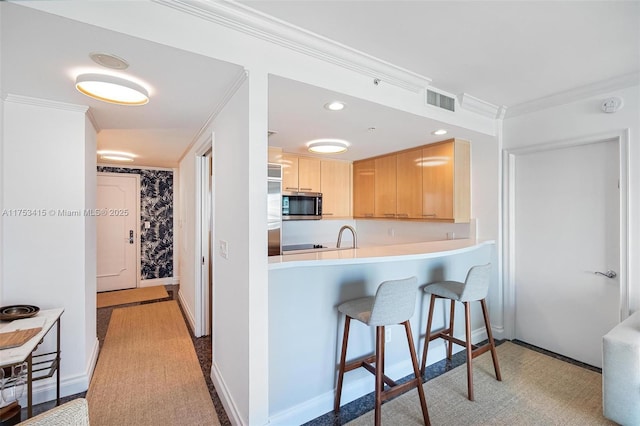 kitchen featuring light brown cabinets, visible vents, ornamental molding, stainless steel microwave, and a kitchen bar