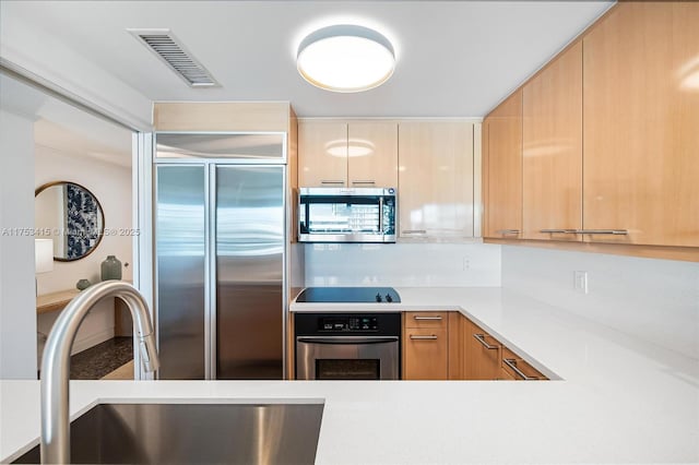 kitchen featuring appliances with stainless steel finishes, visible vents, a sink, and light brown cabinetry