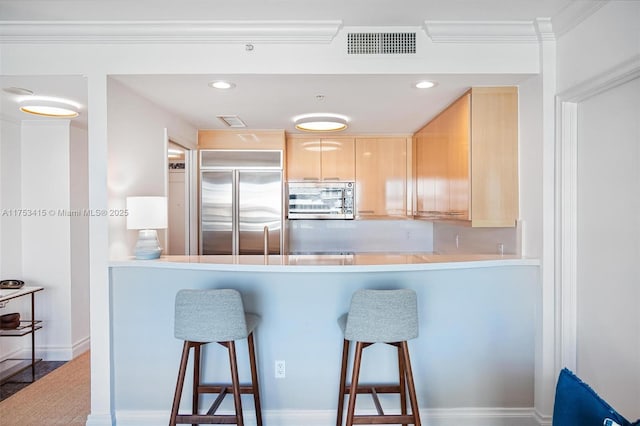 kitchen featuring a breakfast bar, light brown cabinets, visible vents, and stainless steel appliances